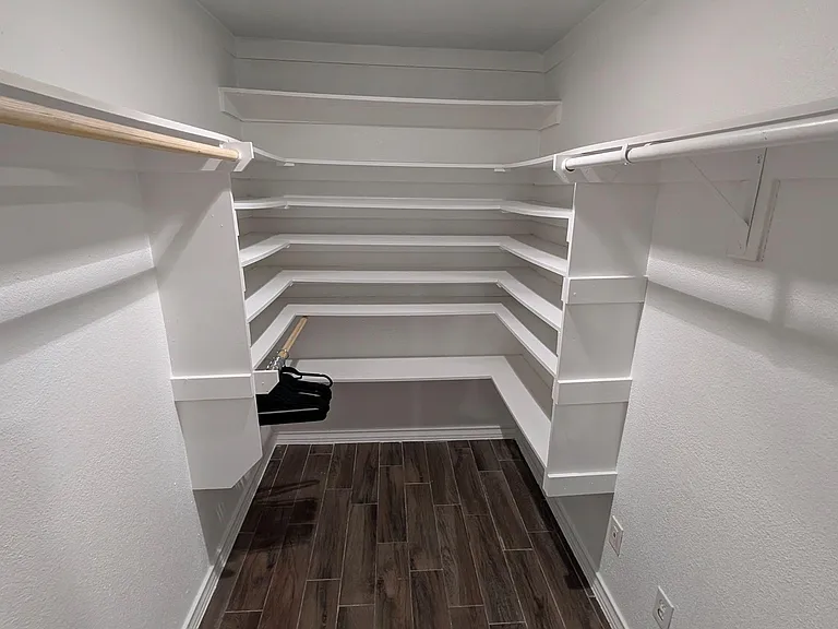 Walk-in storage closet featuring built-in wraparound shelving and hanging rods, plus durable tile-style flooring.