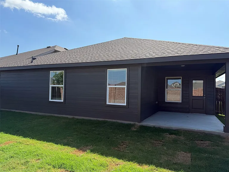 Rear exterior featuring dark horizontal siding, a covered patio with concrete flooring, and multiple windows with white trim