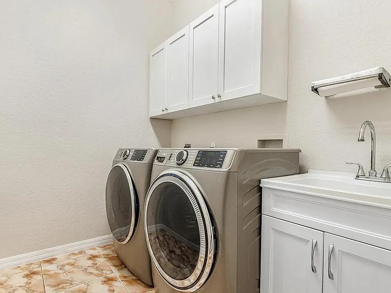 Dedicated laundry room with front-load washer/dryer, overhead cabinetry for storage, and a utility sink for easy cleanup.