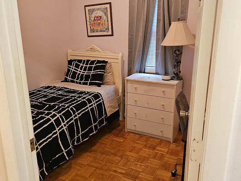Furnished bedroom featuring a twin bed, dresser for storage, and a window with curtains for privacy and light control.