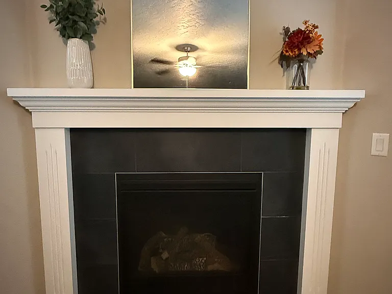 Cozy gas fireplace with classic white mantel, dark gray tile surround.