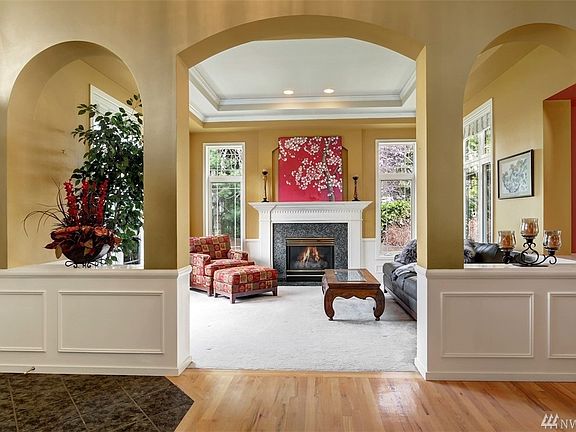 The formal living room to the left boasting a tall ceiling with double crown molding, wainscoting and granite surround gas fireplace.