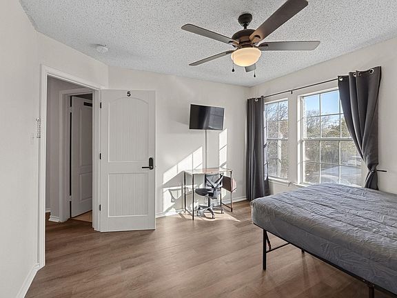 Bedroom with comfortable bed, a mini fridge, a TV, and a work desk. A closet & a ceiling fan.