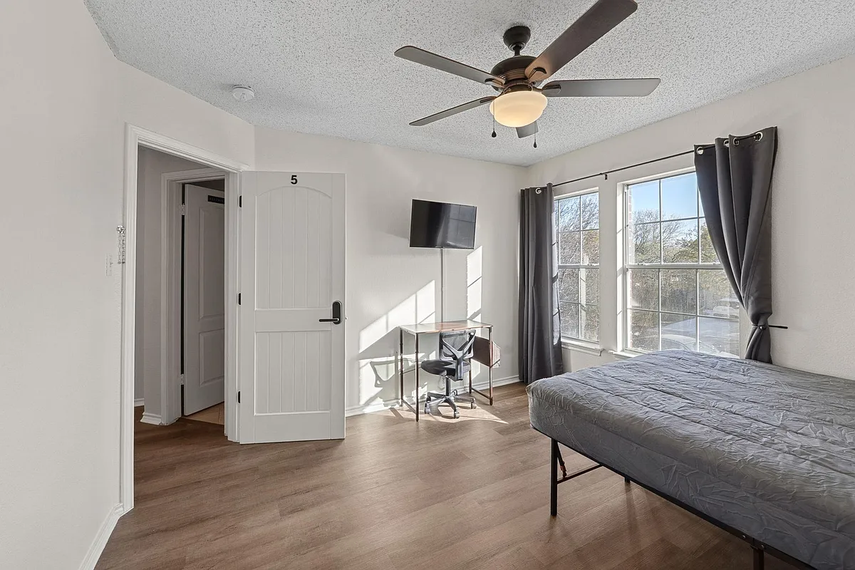 Bedroom with comfortable bed, a mini fridge, a TV, and a work desk. A closet & a ceiling fan. - Fairfield Dr