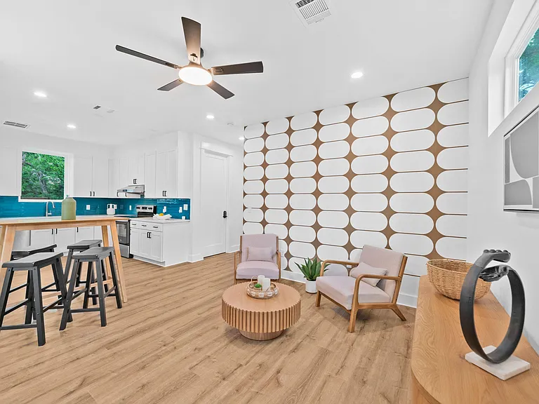 Open-concept living area with lounge seating, ceiling fan, and a kitchen featuring ample cabinetry and an island bar.