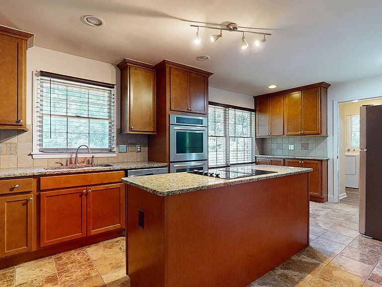 Well-appointed kitchen with ample wood cabinetry, granite counters, and a center island cooktop plus built-in oven.