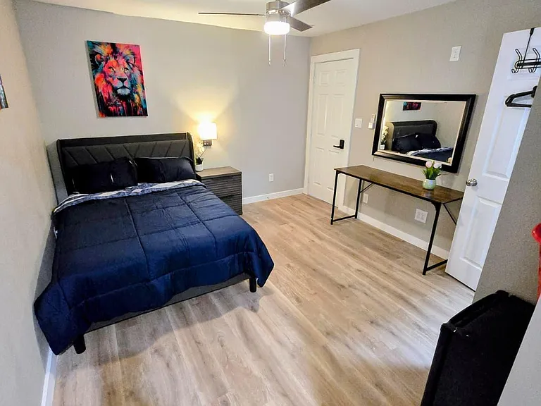 Furnished bedroom with a full bed, nightstand lighting, and a dedicated desk with mirror for getting ready or working.
