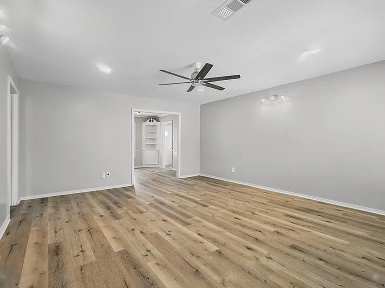 Spacious living room with neutral soft grey paint, LVP flooring, recessing lighting, a ceiling fan and ample amount of light from the large window.