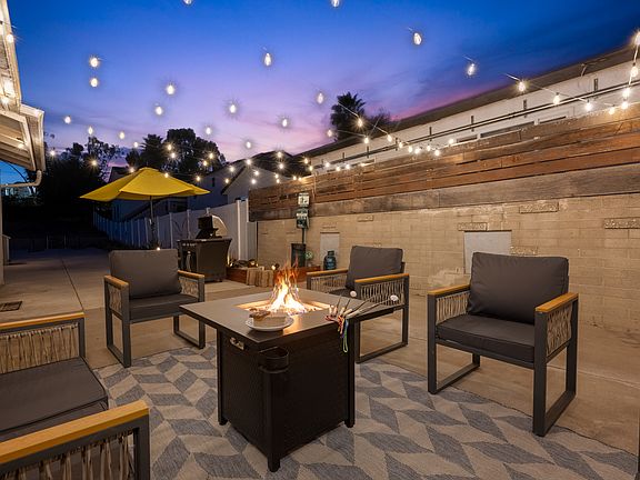 Stunning outdoor space is designed for relaxation and entertainment. A cozy fire pit takes center stage, surrounded by modern outdoor chairs with sleek black cushions and wooden armrests.