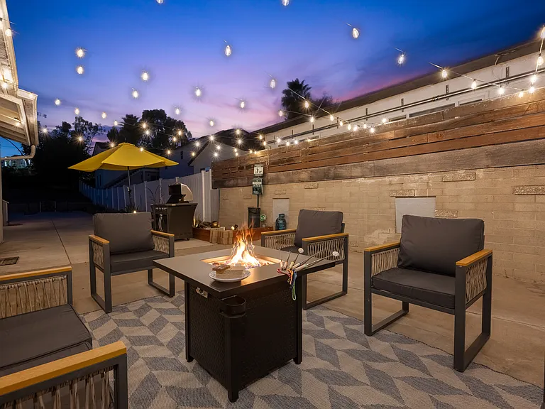 Stunning outdoor space is designed for relaxation and entertainment. A cozy fire pit takes center stage, surrounded by modern outdoor chairs with sleek black cushions and wooden armrests.