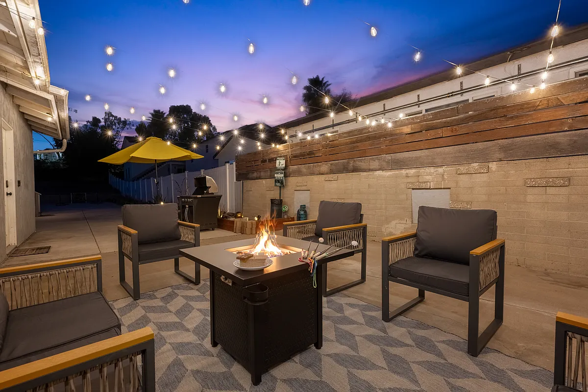 Stunning outdoor space is designed for relaxation and entertainment. A cozy fire pit takes center stage, surrounded by modern outdoor chairs with sleek black cushions and wooden armrests. - 730 Cotton St