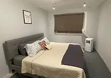 Furnished bedroom featuring a queen bed, upholstered headboard, side table, and window with blinds for light control.