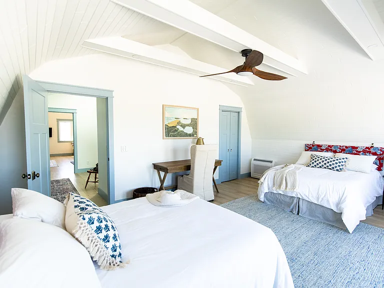 The second bedroom includes two full beds, two small dressers, a closet, a desk, and French doors that open out to the expansive back deck that overlooks vineyards.