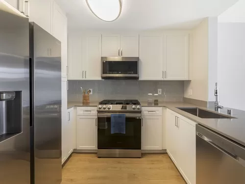 Renovated Package I kitchen with white cabinetry, grey quartz countertops, grey tile backsplash, stainless steel appliances, and hard surface flooring - Avalon Oak Creek