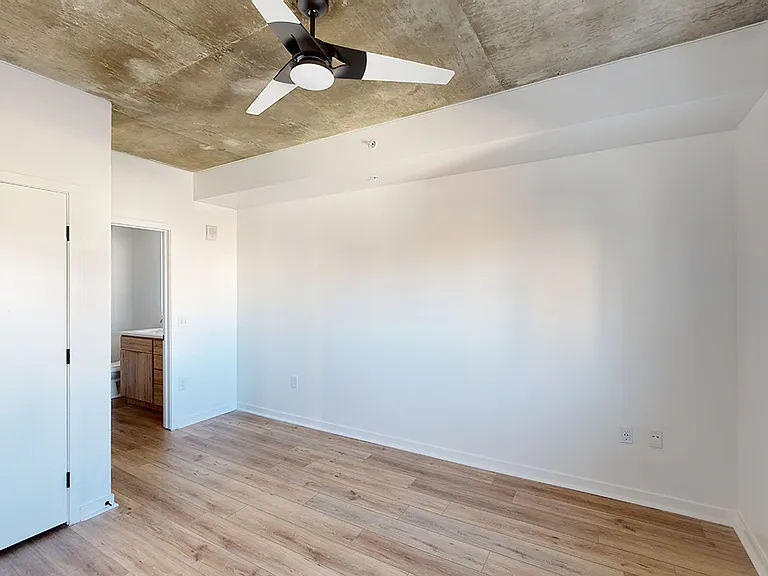 Spacious apartment bedroom with large closet, attached bathroom and wood-style flooring.
