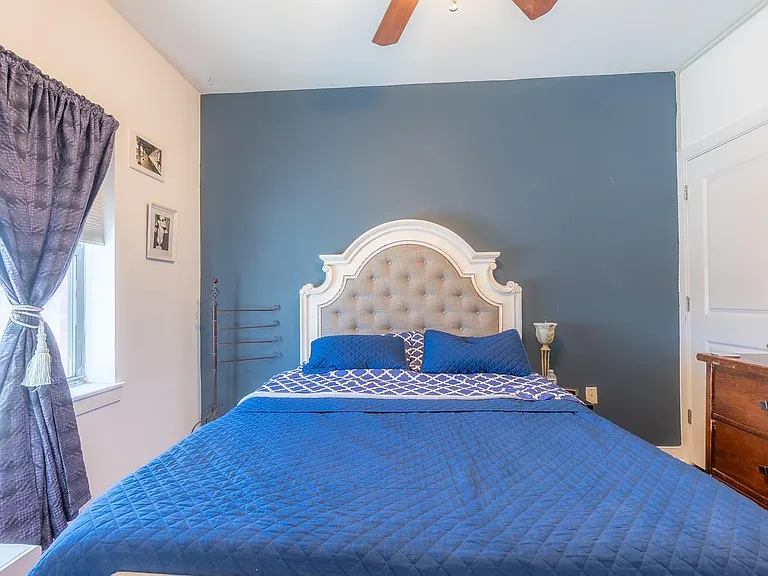 Bedroom features a queen bed, ceiling fan, and window with curtains, plus a dresser for convenient storage.