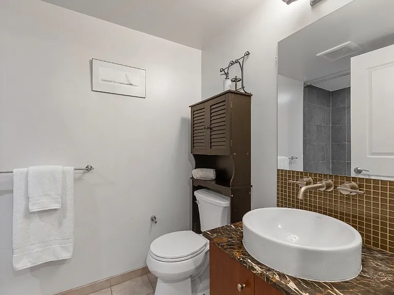 A clean and contemporary guest bathroom featuring a stylish vessel sink, warm gold tile accents, and convenient storage.