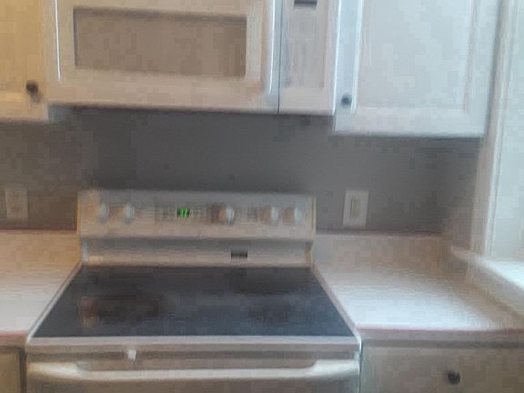 new micro wave, glass top electric range, and cabinets besid