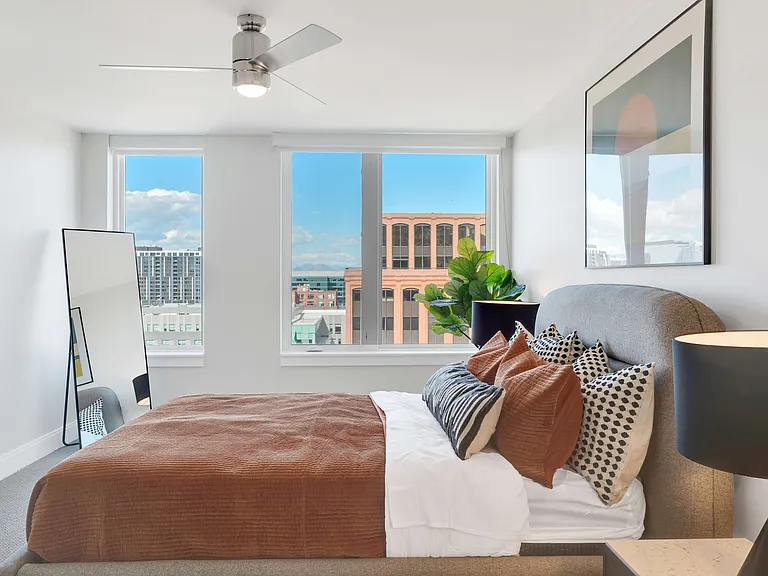 Bright and airy bedroom with a modern aesthetic, showcasing floor-to-ceiling windows with a stunning city view, stylish decor, and plush bedding for a cozy, inviting atmosphere.