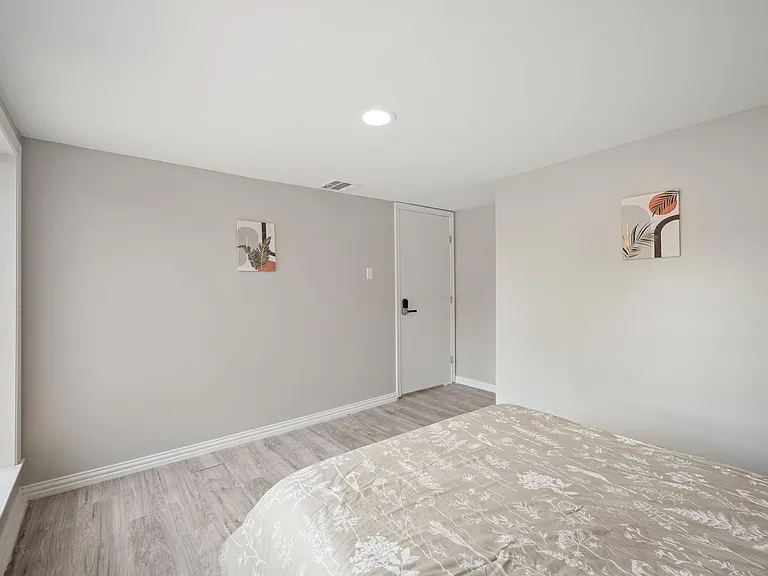 Bedroom with wood-look flooring, neutral walls, and a window for natural light, plus a secure entry door and ceiling light.