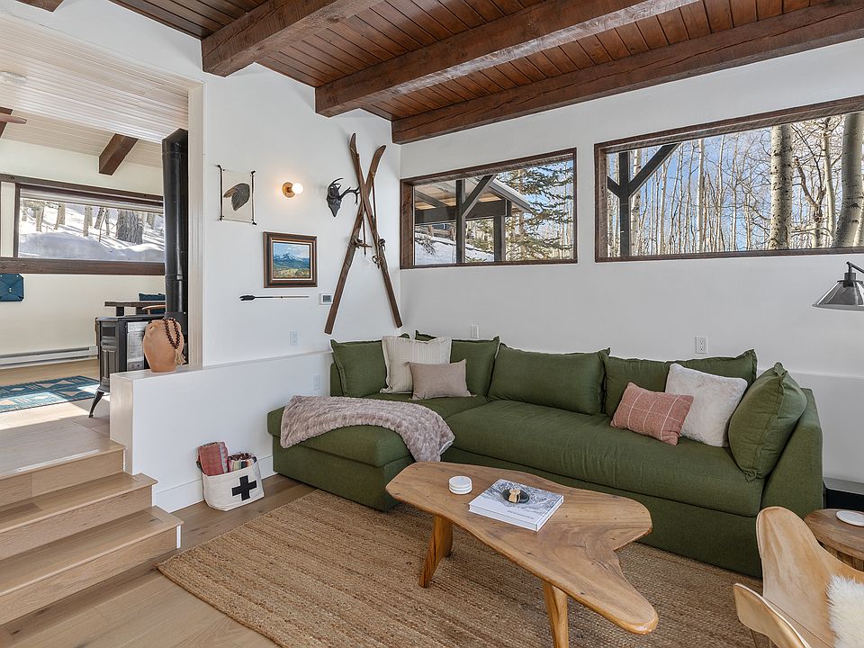 Living room with sectional couch and chair, lighting and a flat screen TV with sound bar, high windows and ceiling with nice light filled ambiance.