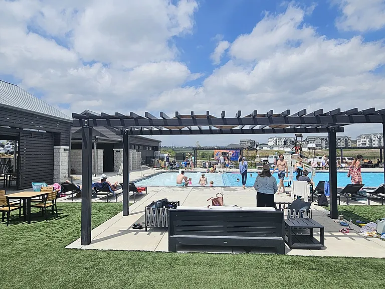 A portion of the community pool that has splash pad, hot tub, and lots of seating, grilling areas, and covered tables