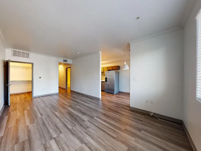 Apartment kitchen with stainless steel appliances, dining and living room with wood-style flooring.