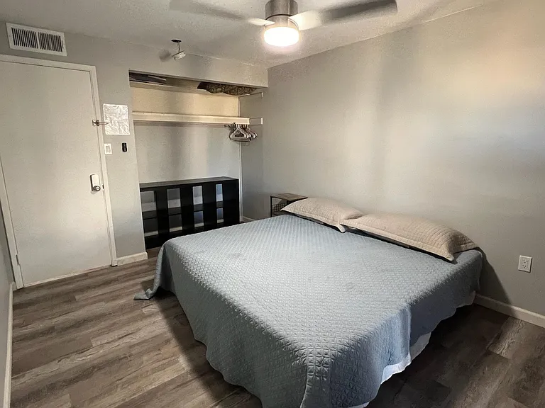 Furnished bedroom with a comfortable bed, ceiling fan, and convenient open closet storage for easy organization.