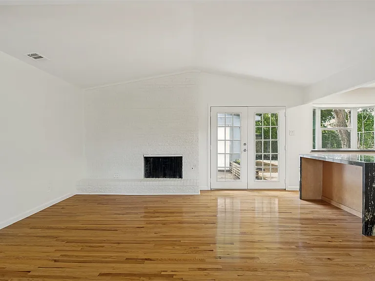 Spacious interior featuring wood-finish flooring, a white brick fireplace, vaulted ceiling, and French doors