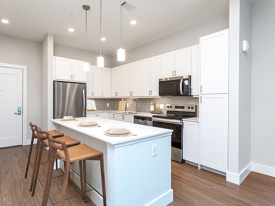 Modern kitchen with white cabinetry, undercabinet lighting, grey tile backsplash, and white quartz countertops