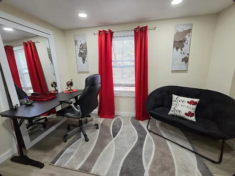 Flexible bonus room with a work desk, futon seating, and a window dressed with curtains for added privacy.