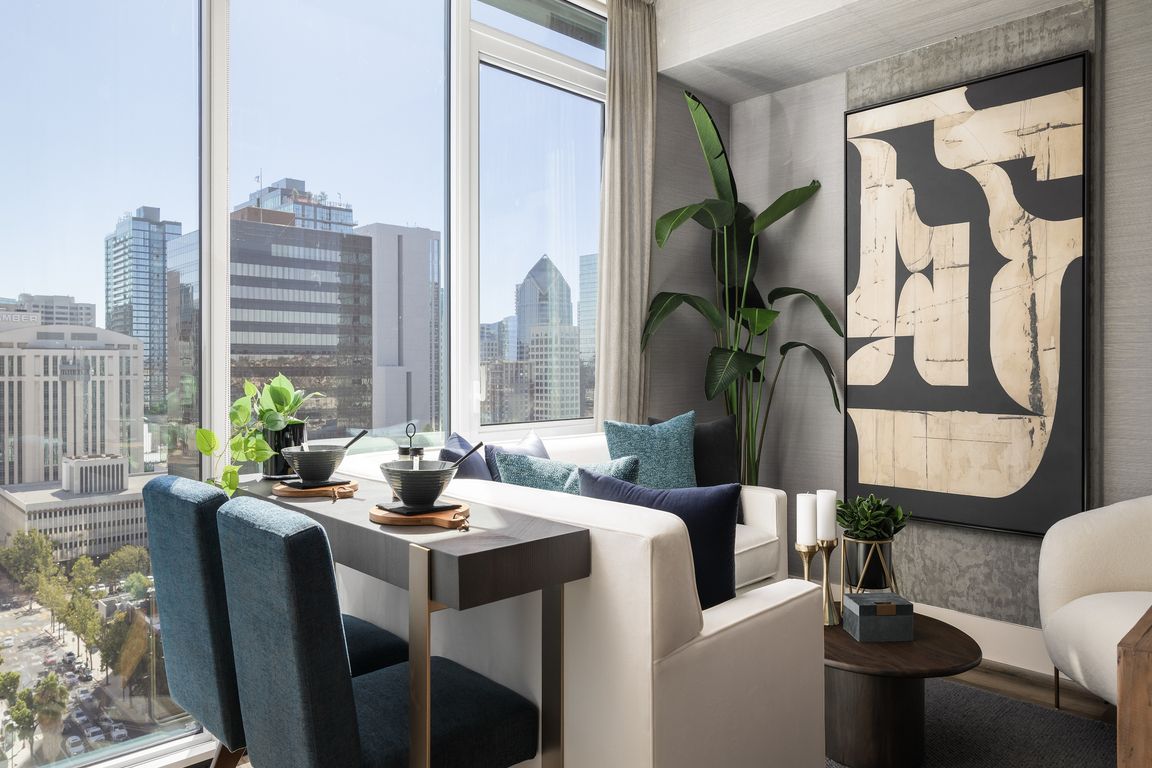Modern apartment interior with elegant dining area, plush seating, and panoramic city views through large windows.