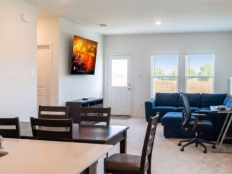 Open-concept living and dining area with a mounted TV, comfortable seating, and a work desk near large windows and patio door