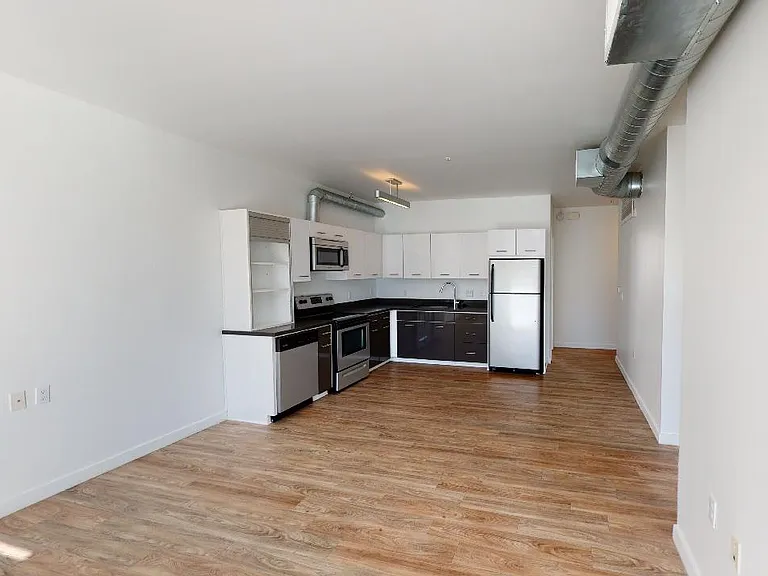 Apartment kitchen with stainless steel appliances, dining and living room with wood-style flooring.