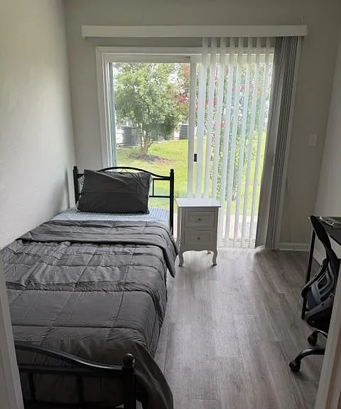 Furnished bedroom with a twin bed, desk space, and sliding glass doors opening to a yard for easy outdoor access.