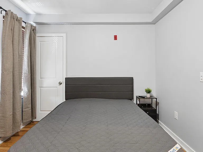 Bedroom with a full-size bed, wood-style flooring, and a window with curtains for light and privacy.