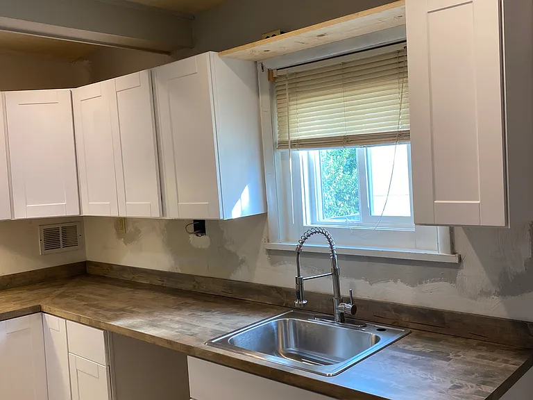 New kitchen layout with new white shaker cabinets and new butcher block counters, new sink and faucet.