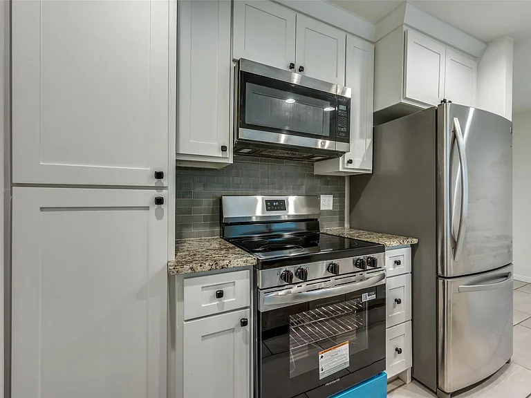 Modern kitchen featuring white shaker cabinetry, stainless steel appliances, granite-style countertops, and a gray subway tile backsplash