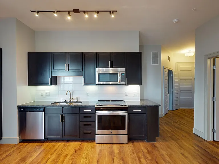 Apartment kitchen with stainless steel appliances, granite countertops, and wood-style flooring.