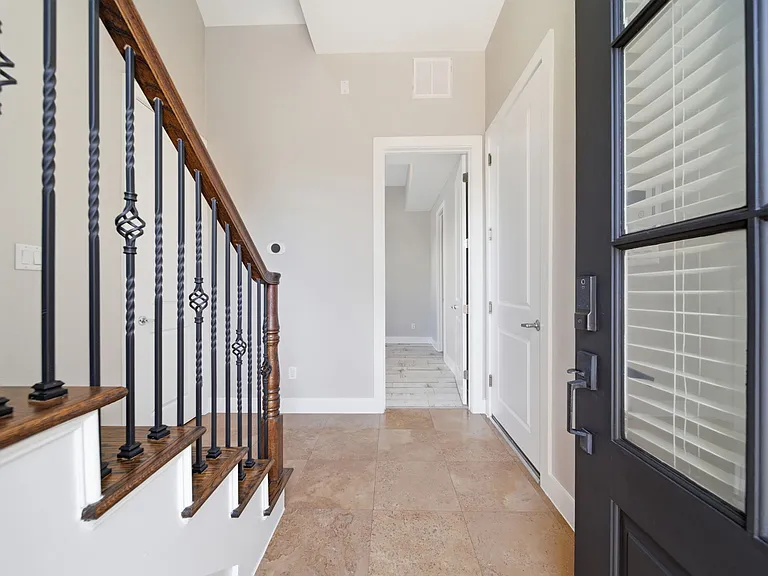 Welcoming entryway featuring a modern black front door with glass panels that allow for natural light. The space opens to tiled flooring and a bright hallway with white interior doors. A convenient coat closet is located to the left.