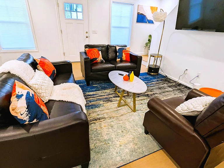 Shared living area with multiple leather seating options, an area rug, and wall-mounted TVideal for relaxing or gathering.