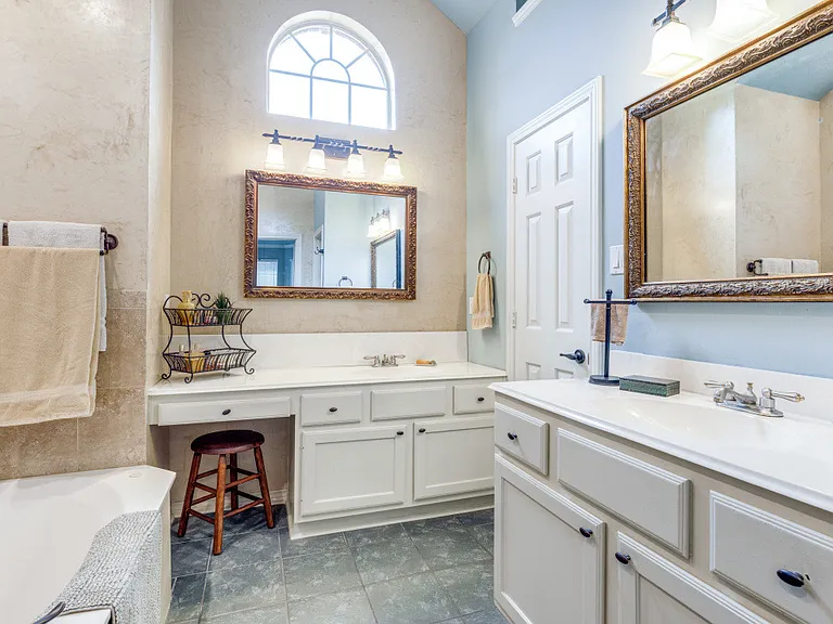 Primary bathroom with vaulted ceiling, arched window, vanities and garden tub.
