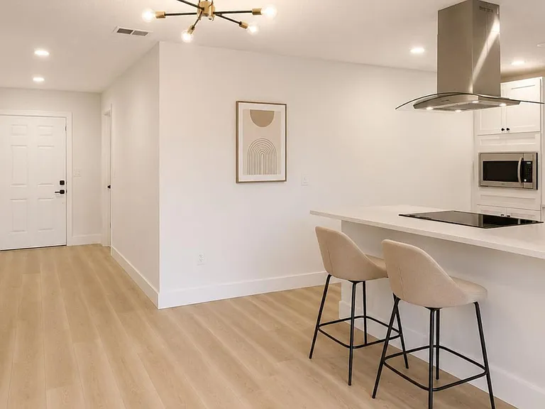 Open kitchen with a large peninsula breakfast bar, built-in microwave, and sleek vent hood over a smooth cooktop.
