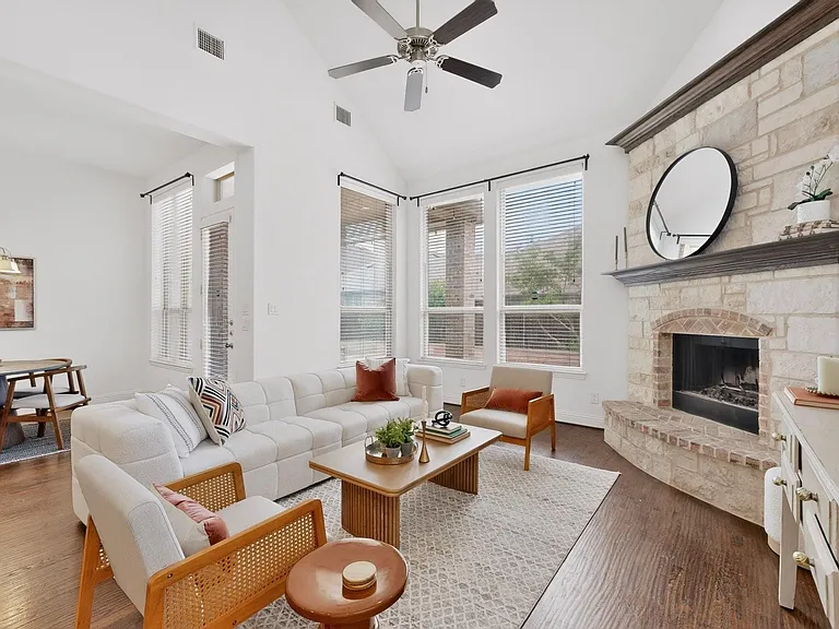 Bright living room showcasing a fireplace, tall windows, and a ceiling fan, creating a welcoming space.