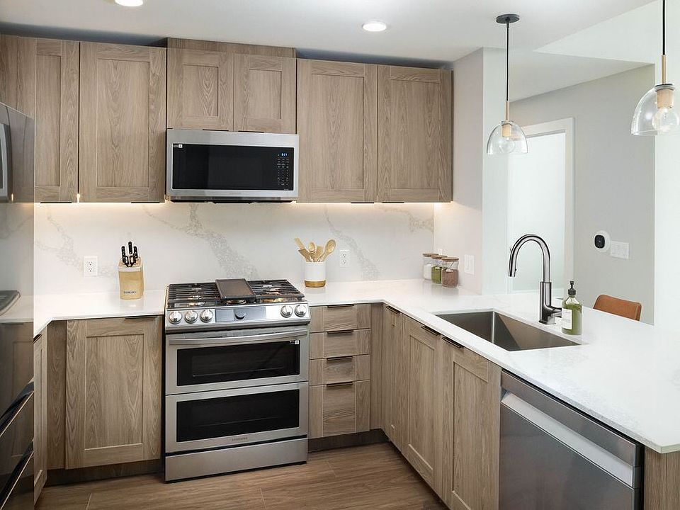Signature Collection kitchen with stainless steel appliances, marbled white quartz countertops, brown cabinetry, and hard surface vinyl plank flooring (Representative photo)
