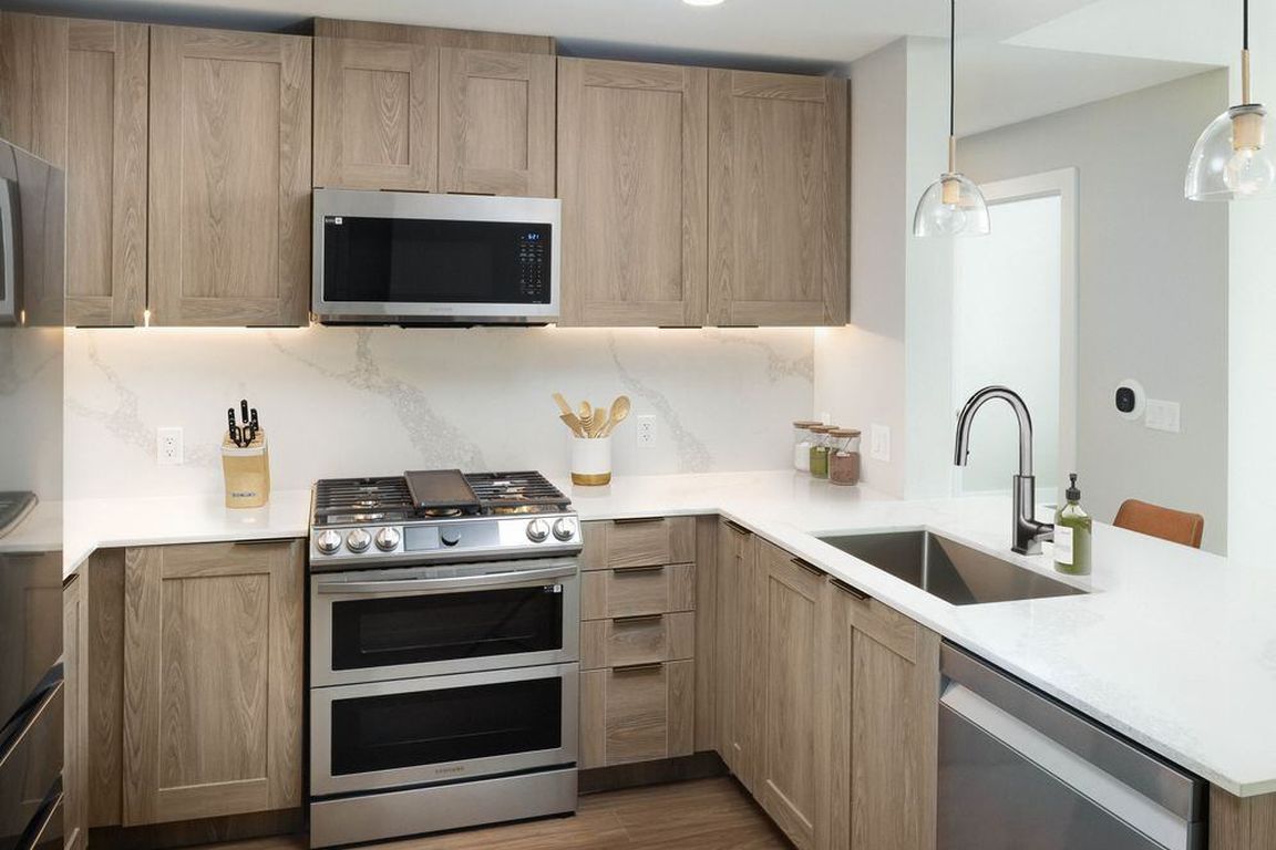 Signature Collection kitchen with stainless steel appliances, marbled white quartz countertops, brown cabinetry, and hard surface vinyl plank flooring (Representative photo)