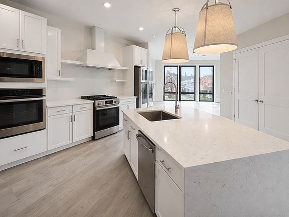 Modern chef's kitchen with quartz waterfall island, custom white cabinetry, and stainless steel appliances. Gas range, wall oven, tile backsplash, and designer pendant lighting. Bright, open layout with abundant natural light_ideal for cooking and enterta