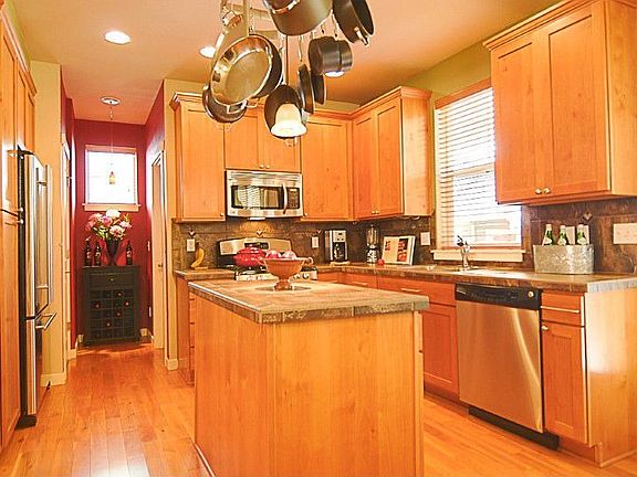 Kitchen has a great open layout and features light maple cabinets, tiled counters, gas range, all stainless appliances, center Island with hanging pot rack, and walk-in pantry.