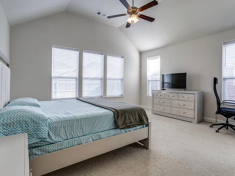 Carpeted bedroom featuring ceiling fan, vaulted ceiling, and multiple windows