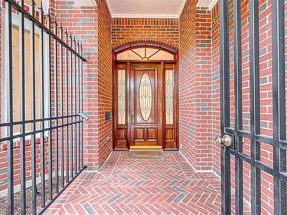 Stunning covered porch featuring handsome rich wood front door with attractive lead paned glass. Notice the ornate herringbone brick flooring. The porch is surrounded by a wrought iron fence with locking door providing additional security.